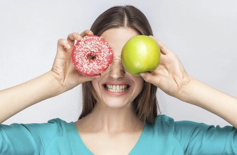 mujer sujetando un donut y una manzana cada uno en un ojo